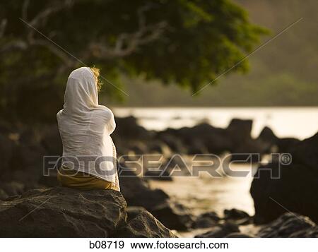 Rear view of a woman sitting on a rock View Large Photo Image Stock Photo - Rear view of a woman sitting on a rock. Fotosearch