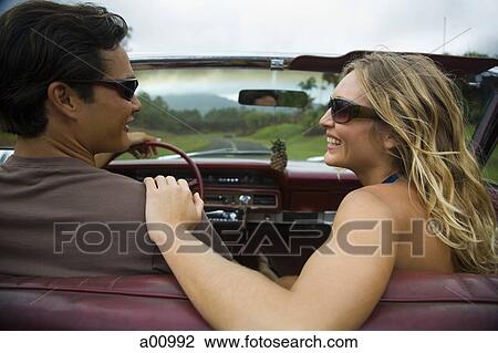 Stock Image - Rear view of a young couple sitting in a car. Fotosearch