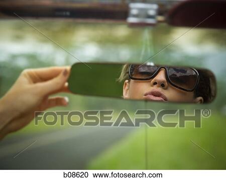 Stock Image - Reflection of a young woman in a rear view mirror. Fotosearch