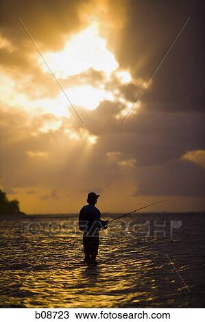 Stock Image - Silhouette of a man fly-fishing at dusk. Fotosearch