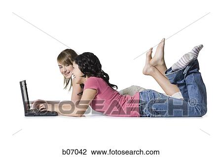Stock Image - Teenage friends lying on table with laptop. Fotosearch