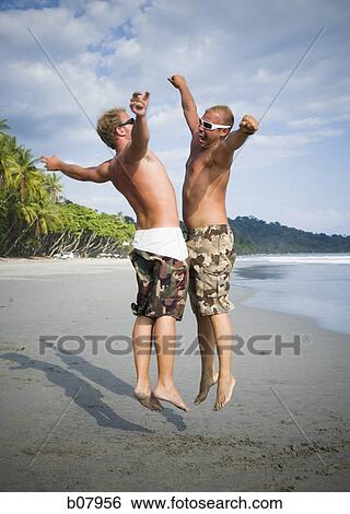 Two males jumping on the beach View Large Photo Image Stock Photograph - Two males jumping on the beach. Fotosearch