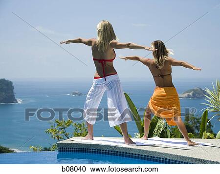 Two women performing yoga exercises by infinity pool View Large Photo Image Stock Image - Two women performing yoga exercises by infinity pool. Fotosearch