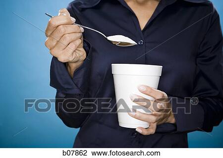 Stock Image - Woman adding sugar to her beverage. Fotosearch