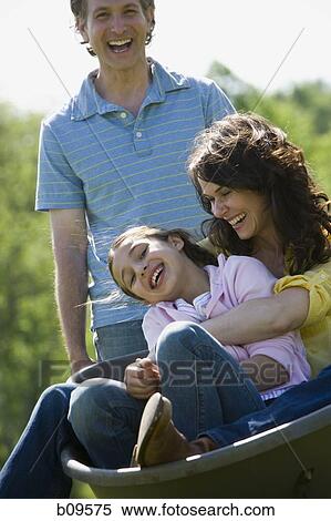 Stock Photography - woman and her daughter sitting in a wheel barrow with a man standing beside them. Fotosearch