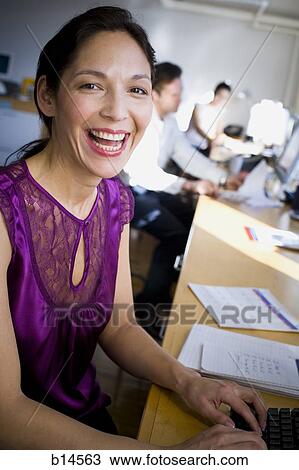 Woman at desk with keyboard in open office smiling View Large Photo Image Stock Image - Woman at desk with keyboard in open office smiling. Fotosearch
