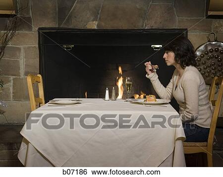 Woman dining alone in front of fireplace View Large Photo Image Stock Photograph - Woman dining alone in front of fireplace. Fotosearch