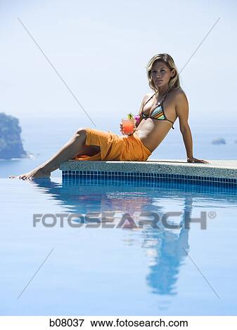 Stock Photo - Woman relaxing by infinity pool. Fotosearch