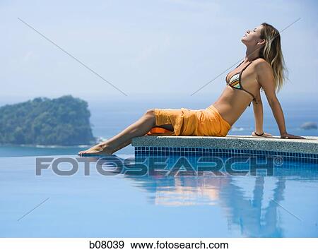 Stock Photo - Woman relaxing by infinity pool. Fotosearch