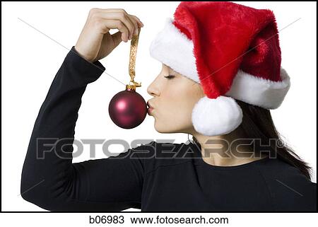 Stock Image - Woman with santa hat kissing christmas ornament. Fotosearch