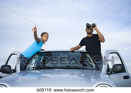 Stock Photo - Young man and a young woman standing near a car. Fotosearch