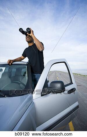 Stock Image - Young man looking through a pair of binoculars. Fotosearch