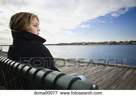 Young woman sitting on waterfront View Large Photo Image Stock Photo - Young woman sitting on waterfront. Fotosearch