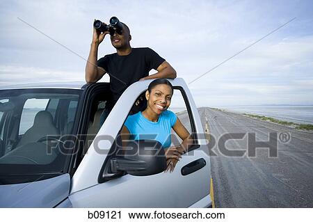 Stock Image - Young woman smiling with a young man looking through a pair of binoculars. Fotosearch