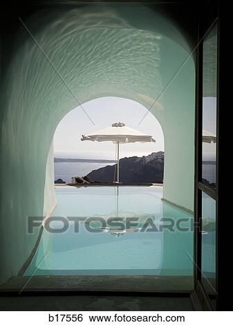 Stock Photograph - Arch with infinity pool and ocean with black rock and umbrella. Fotosearch