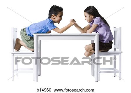 Stock Image - Boy and girl sitting at table arm wrestling. Fotosearch