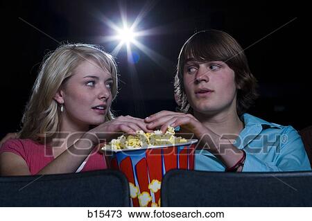 Stock Image - Boy and girl touching hands in popcorn at movie theater. Fotosearch