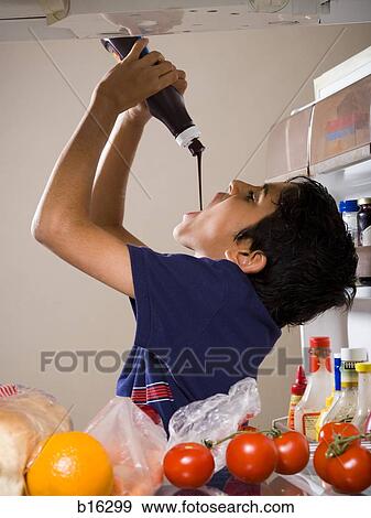 Stock Photo - Boy drinking chocolate syrup from bottle in refrigerator. Fotosearch