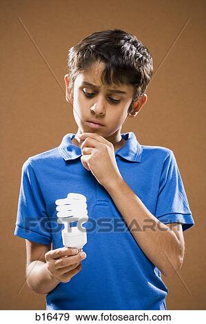 Boy holding energy efficient lightbulb thinking View Large Photo Image Stock Photo - Boy holding energy efficient lightbulb thinking. Fotosearch