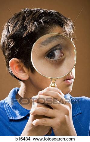 Boy holding magnifying glass to eye View Large Photo Image Picture - Boy holding magnifying glass to eye. Fotosearch