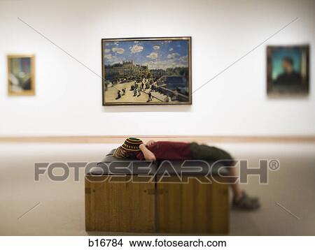 Boy Laying Down On Bench In Art Gallery With Hat Covering Face