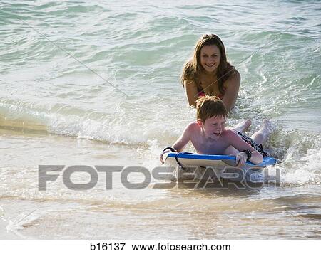 Boy on surfboard in water with woman View Large Photo Image Stock Photo - Boy on surfboard in water with woman. Fotosearch