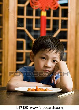 Boy sitting at table looking ambivalent View Large Photo Image Stock Image - Boy sitting at table looking ambivalent. Fotosearch