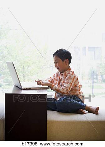 Boy sitting with laptop in front of large window smiling View Large Photo Image Stock Photo - Boy sitting with laptop in front of large window smiling. Fotosearch