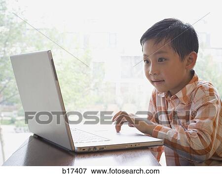 Boy sitting with laptop in front of large window smiling View Large Photo Image Stock Photo - Boy sitting with laptop in front of large window smiling. Fotosearch