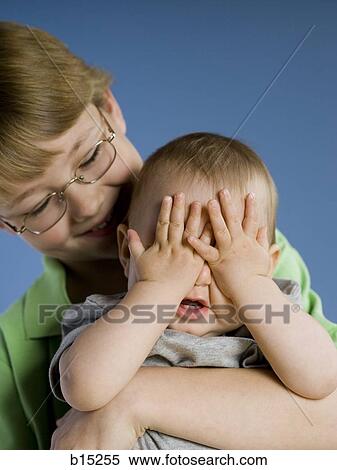 Boy with eyeglasses holding baby with eyes covered View Large Photo Image Stock Photography - Boy with eyeglasses holding baby with eyes covered. Fotosearch