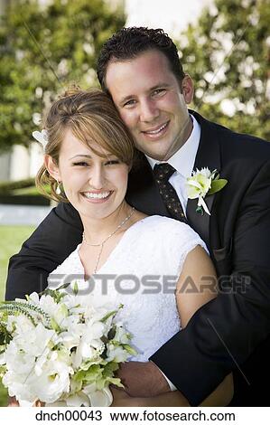 Stock Image - Bride and groom embracing and smiling outdoors. Fotosearch