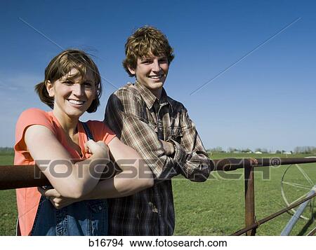 Brother and sister leaning on wooden fence in field with blue skies View Large Photo Image Picture - Brother and sister leaning on wooden fence in field with blue skies. Fotosearch