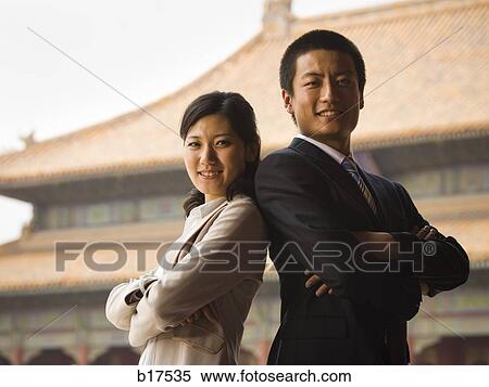Businessman and woman standing with arms crossed and backs together with pagoda in background View Large Photo Image Stock Photography - Businessman and woman standing with arms crossed and backs together with pagoda in background. Fotosearch