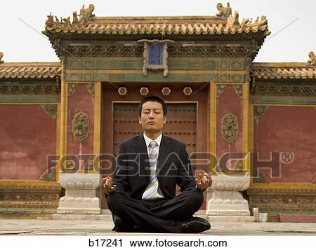 Stock Image - Businessman sitting cross legged outdoors meditating. Fotosearch