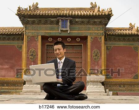 Businessman sitting cross legged outdoors with laptop View Large Photo Image Stock Photograph - Businessman sitting cross legged outdoors with laptop. Fotosearch