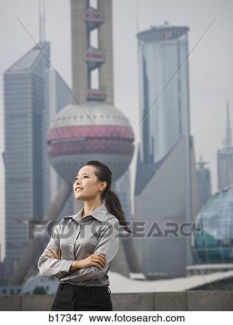 Businesswoman smiling outdoors with arms crossed and city skyline in background View Large Photo Image Stock Photo - Businesswoman smiling outdoors with arms crossed and city skyline in background. Fotosearch