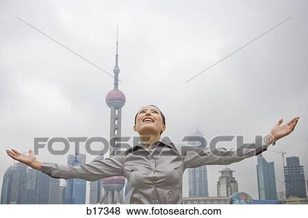 Businesswoman smiling outdoors with arms up and city skyline in background View Large Photo Image Stock Photo - Businesswoman smiling outdoors with arms up and city skyline in background. Fotosearch