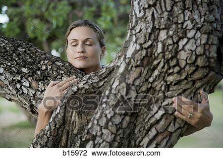 Stock Image - Close-up of woman hugging tree outdoors. Fotosearch