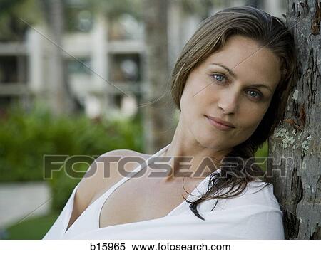 Stock Photography - Close-up of woman leaning on tree outdoors smiling. Fotosearch