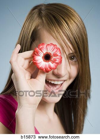 Close-up of woman smiling holding flower up to her eye View Large Photo Image Stock Image - Close-up of woman smiling holding flower up to her eye. Fotosearch