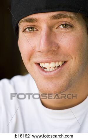 Stock Image - Close-up of young man smiling with cap. Fotosearch