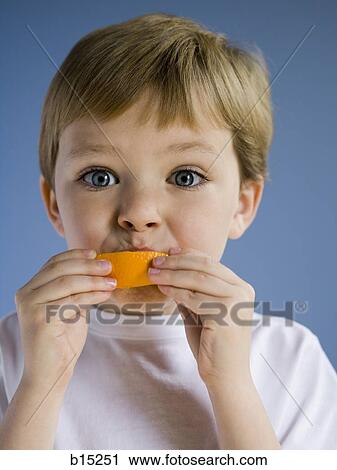 Stock Image - Closeup of boy eating orange wedge. Fotosearch