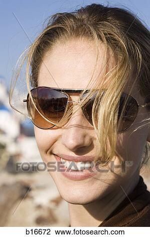 Stock Image - Closeup of woman smiling outdoors with sunglasses. Fotosearch