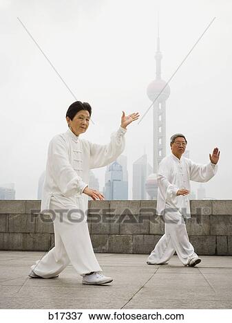 Couple doing tai chi outdoors with city skyline in background View Large Photo Image Stock Photo - Couple doing tai chi outdoors with city skyline in background. Fotosearch