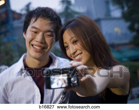 Couple embracing and smiling outdoors with camera View Large Photo Image Stock Photo - Couple embracing and smiling outdoors with camera. Fotosearch