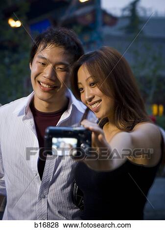 Couple embracing and smiling outdoors with camera View Large Photo Image Stock Photo - Couple embracing and smiling outdoors with camera. Fotosearch