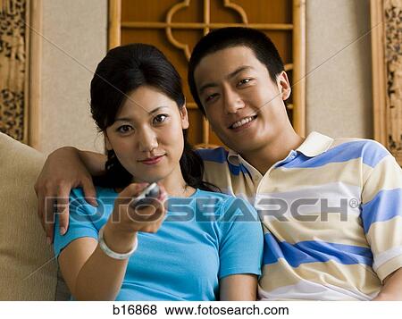Couple embracing on sofa while woman changes channels with television remote View Large Photo Image Stock Photo - Couple embracing on sofa while woman changes channels with television remote. Fotosearch