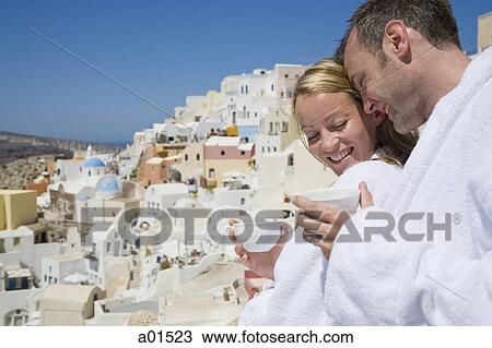 Couple in bathrobes with cups smiling with scenic village in background View Large Photo Image Stock Image - Couple in bathrobes with cups smiling with scenic village in background. Fotosearch