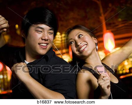Stock Photo - Couple listening to mp3 player outdoors dancing and smiling. Fotosearch