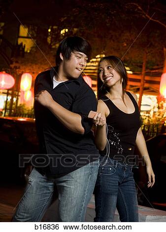 Stock Photograph - Couple listening to mp3 player outdoors dancing and smiling. Fotosearch